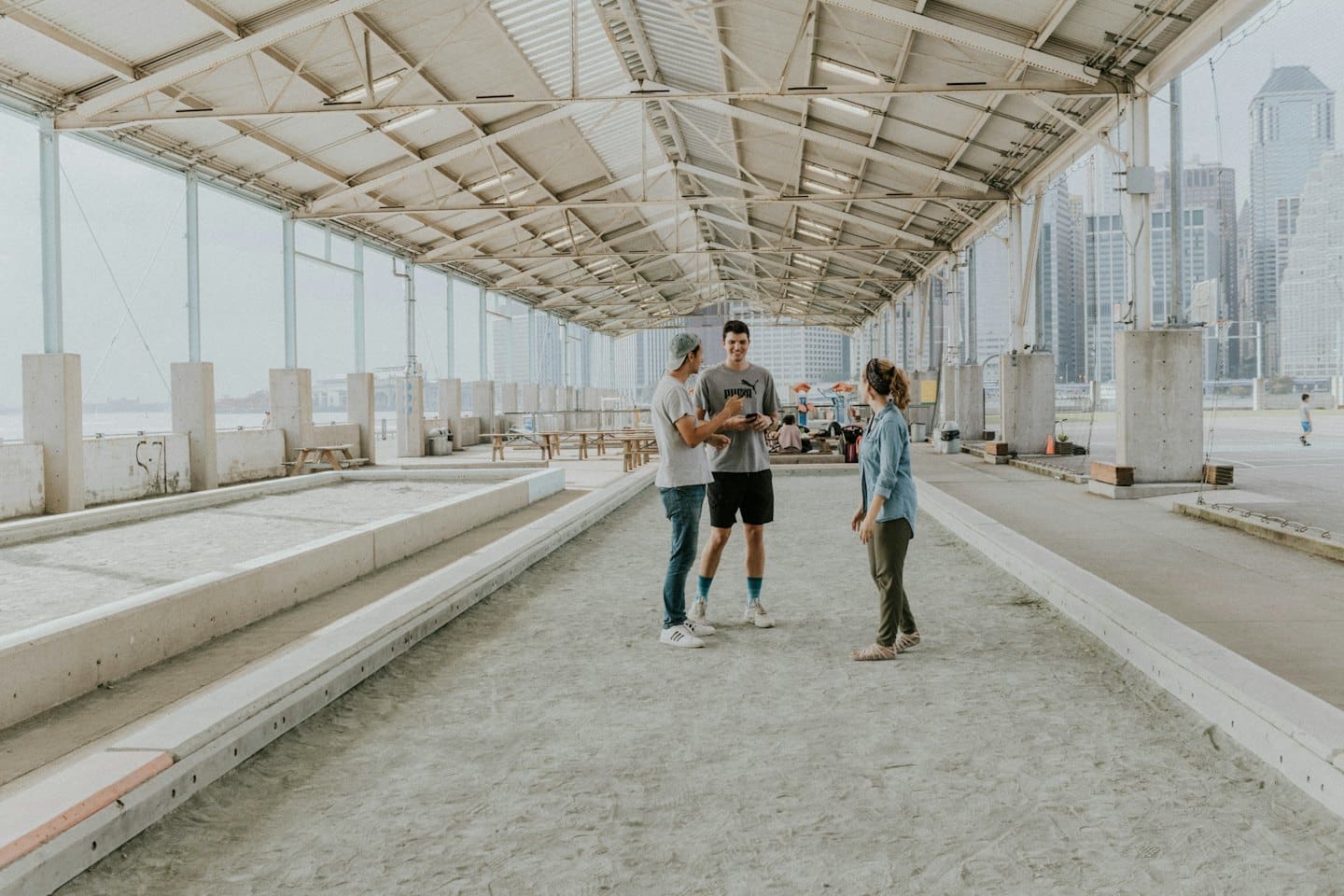 Three young adults look at a smartphone on bocce courts.