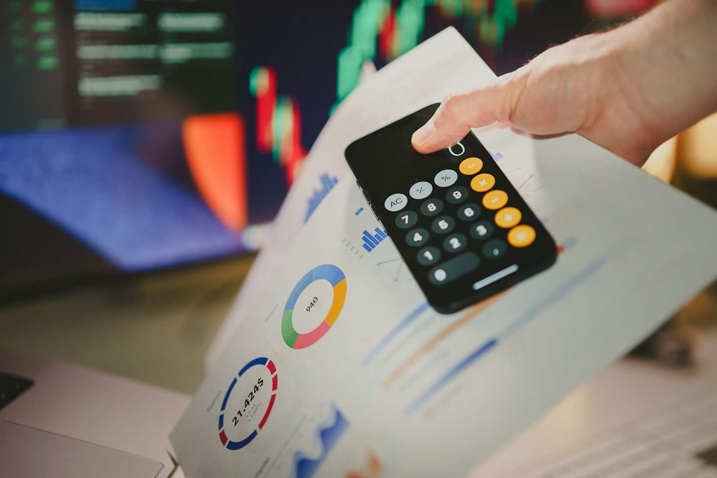 Hand holds smartphone over financial documents and charts.